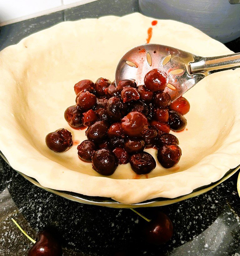 cherry crumble pie spooning filling to assemble pie